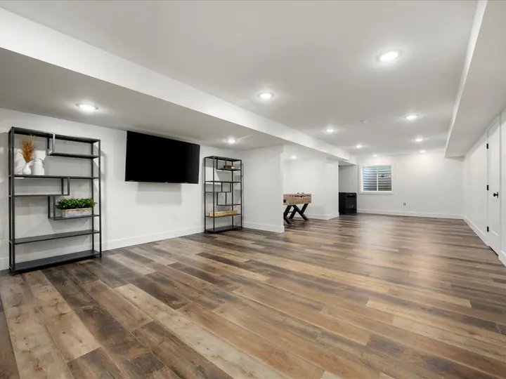 Finished basement with wide-plank flooring and a wall-mounted television