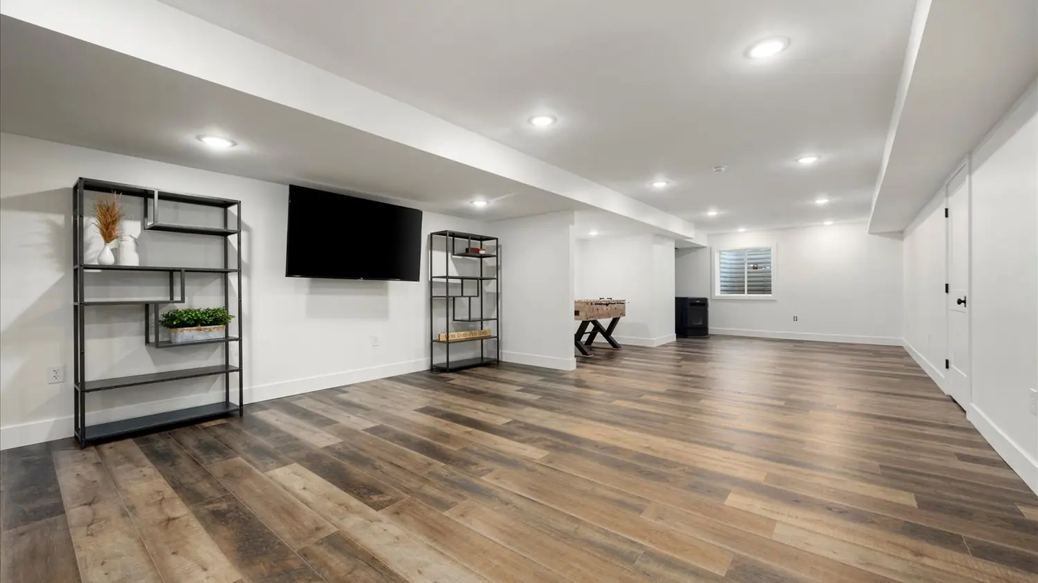 Finished basement with wide-plank flooring and a wall-mounted television